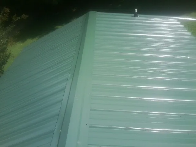 New green metal panels meeting at the ridge of a roof — Flat Roof Repair work by our crew in Jamestown
