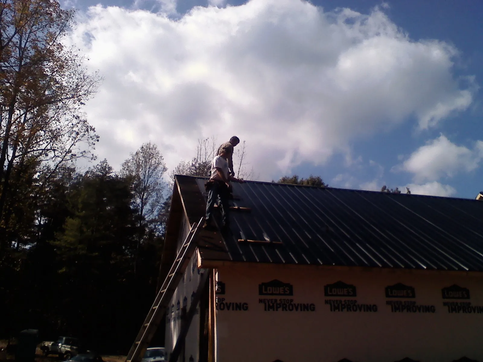 Roofer fastening dark metal panels high against a cloudy sky, from a Roof Inspection job in Jamestown